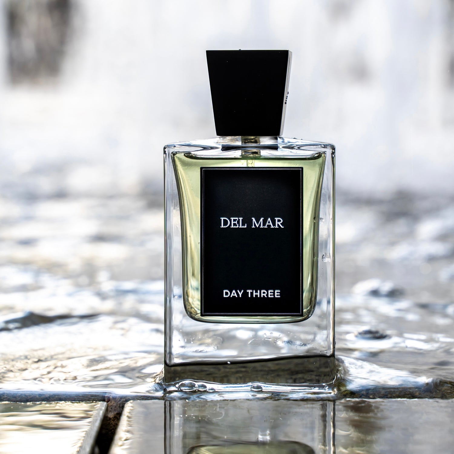 Perfume bottle labeled 'Del Mar Day Three' on a reflective surface with blurred background