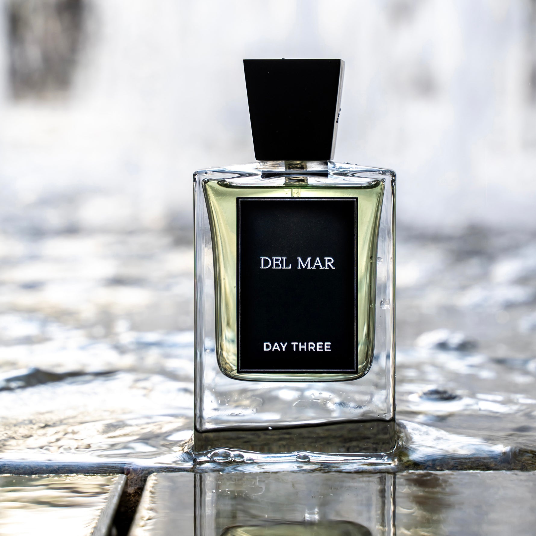 Perfume bottle labeled 'Del Mar Day Three' on a reflective surface with blurred background