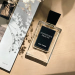 Perfume bottle labeled 'Downtown Deja Vu Day Three' on a beige surface with a magazine and branches in the background.