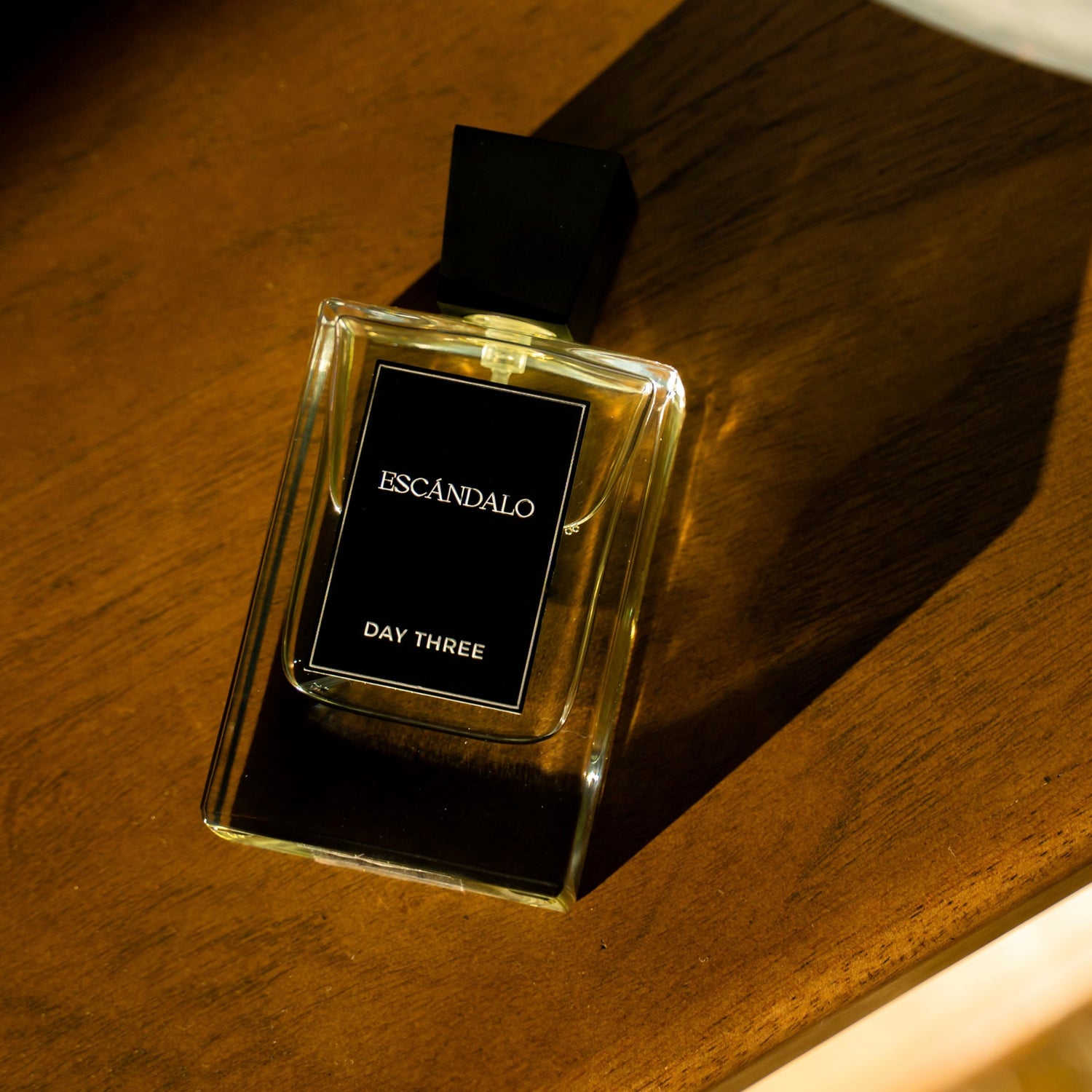 Perfume bottle labeled 'Escandalo Day Three' on a wooden surface