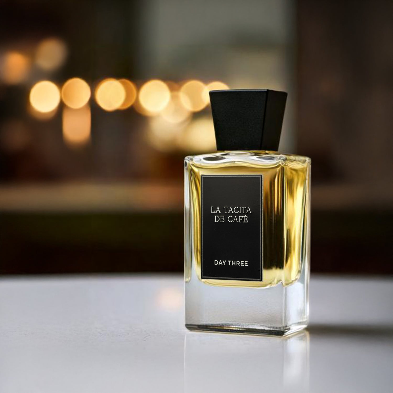 Perfume bottle labeled 'La Tacita de Cafe' on a reflective surface with blurred lights in the background